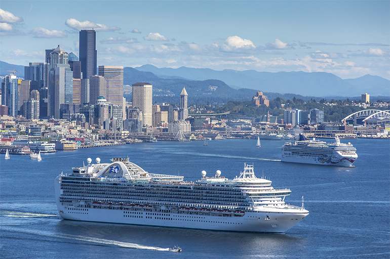 Two cruise ships departing Seattle on a sunny day with the skyline in the background.